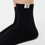 Woman wearing a solid black ankle grip sock with aries zodiac sign embroidered on the side. Made for pilates, barre, yoga, and beyond. 