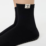 Woman wearing a solid black ankle grip sock with aries zodiac sign embroidered on the side. Made for pilates, barre, yoga, and beyond. 