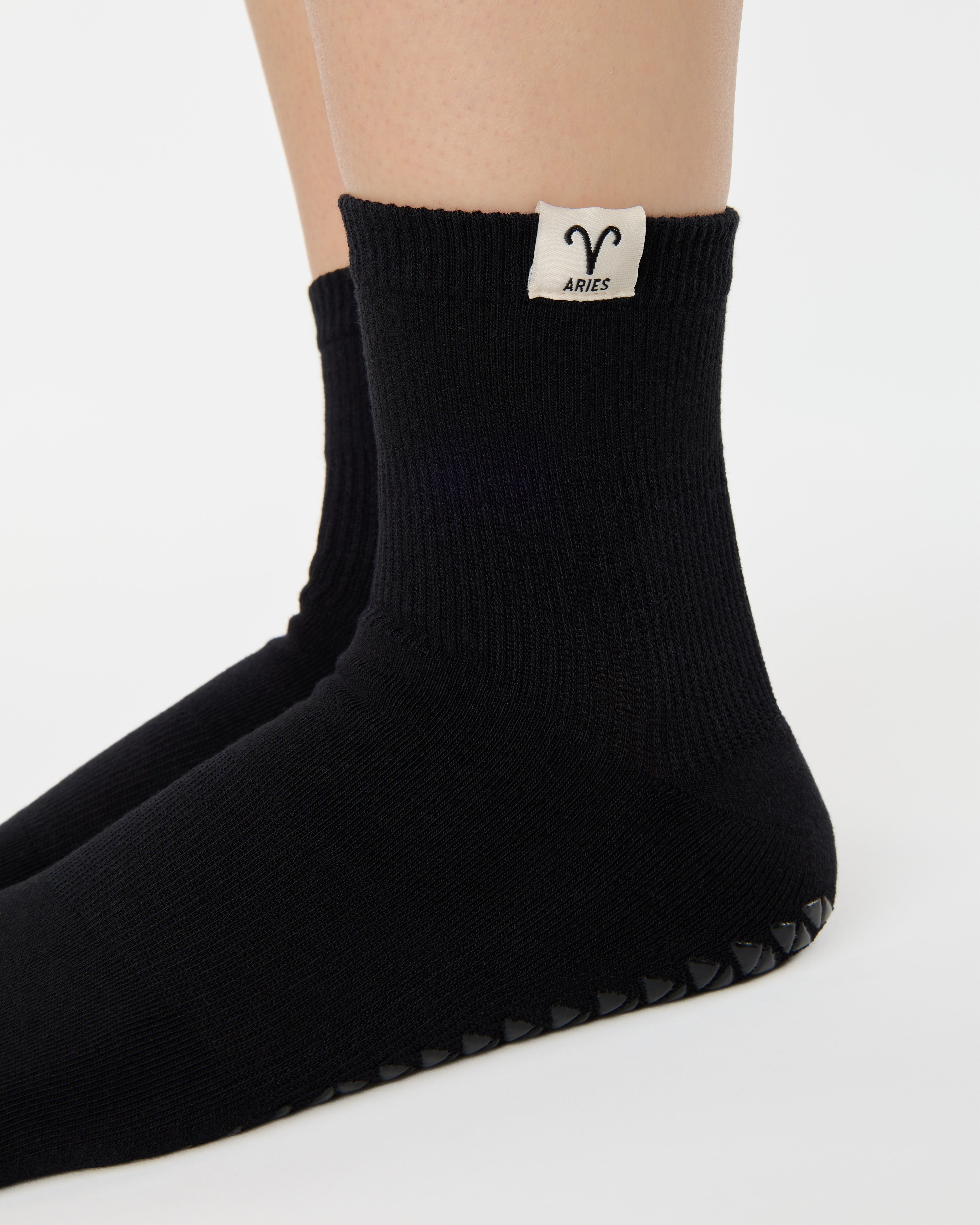 Woman wearing a solid black ankle grip sock with aries zodiac sign embroidered on the side. Made for pilates, barre, yoga, and beyond. 