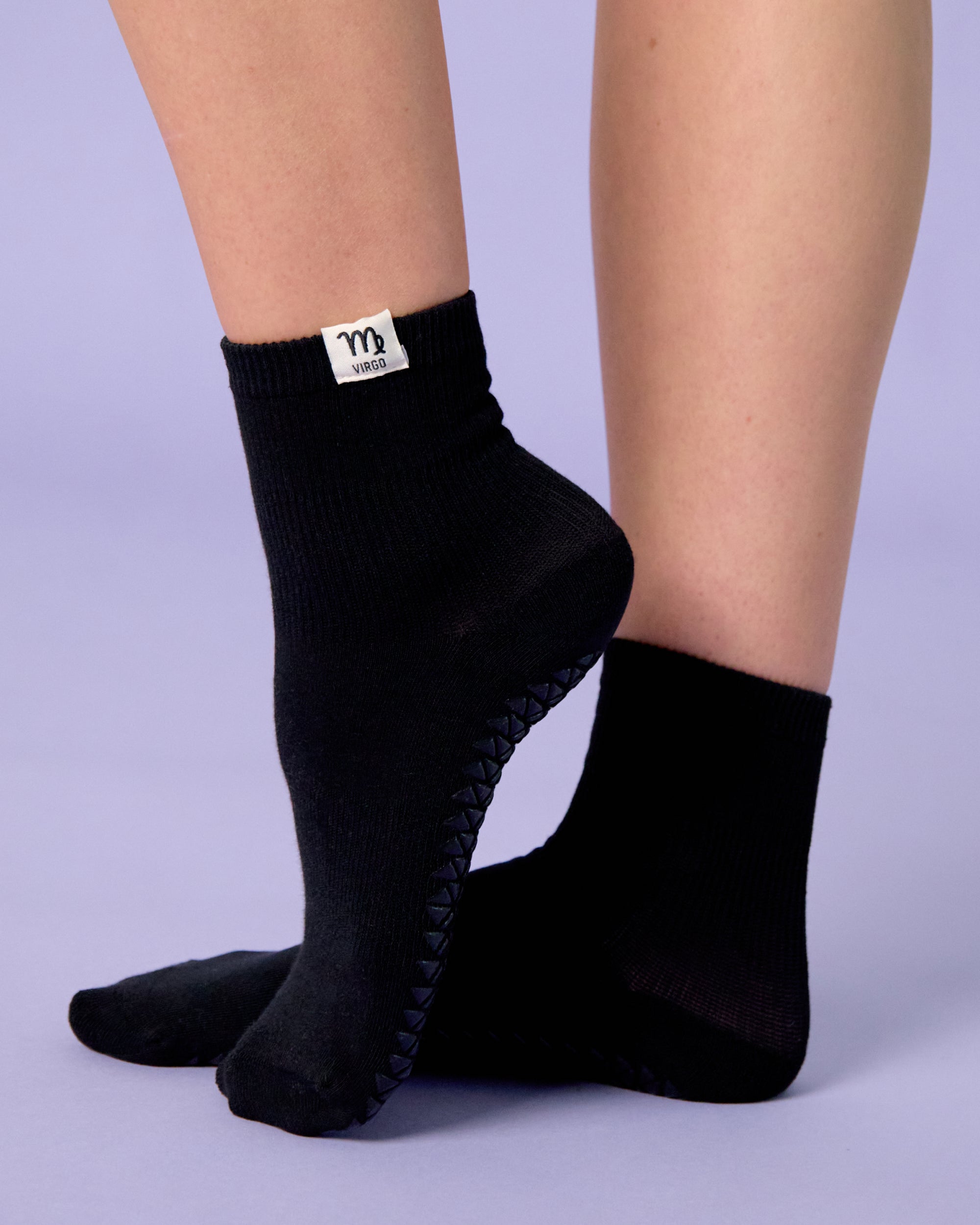 Woman wearing a solid black ankle grip sock with your zodiac sign embroidered on the side. Made for pilates, barre, yoga, and beyond. 