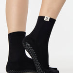Woman wearing a solid black ankle grip sock with cancer zodiac sign embroidered on the side. Made for pilates, barre, yoga, and beyond. 
