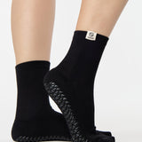 Woman wearing a solid black ankle grip sock with cancer zodiac sign embroidered on the side. Made for pilates, barre, yoga, and beyond. 
