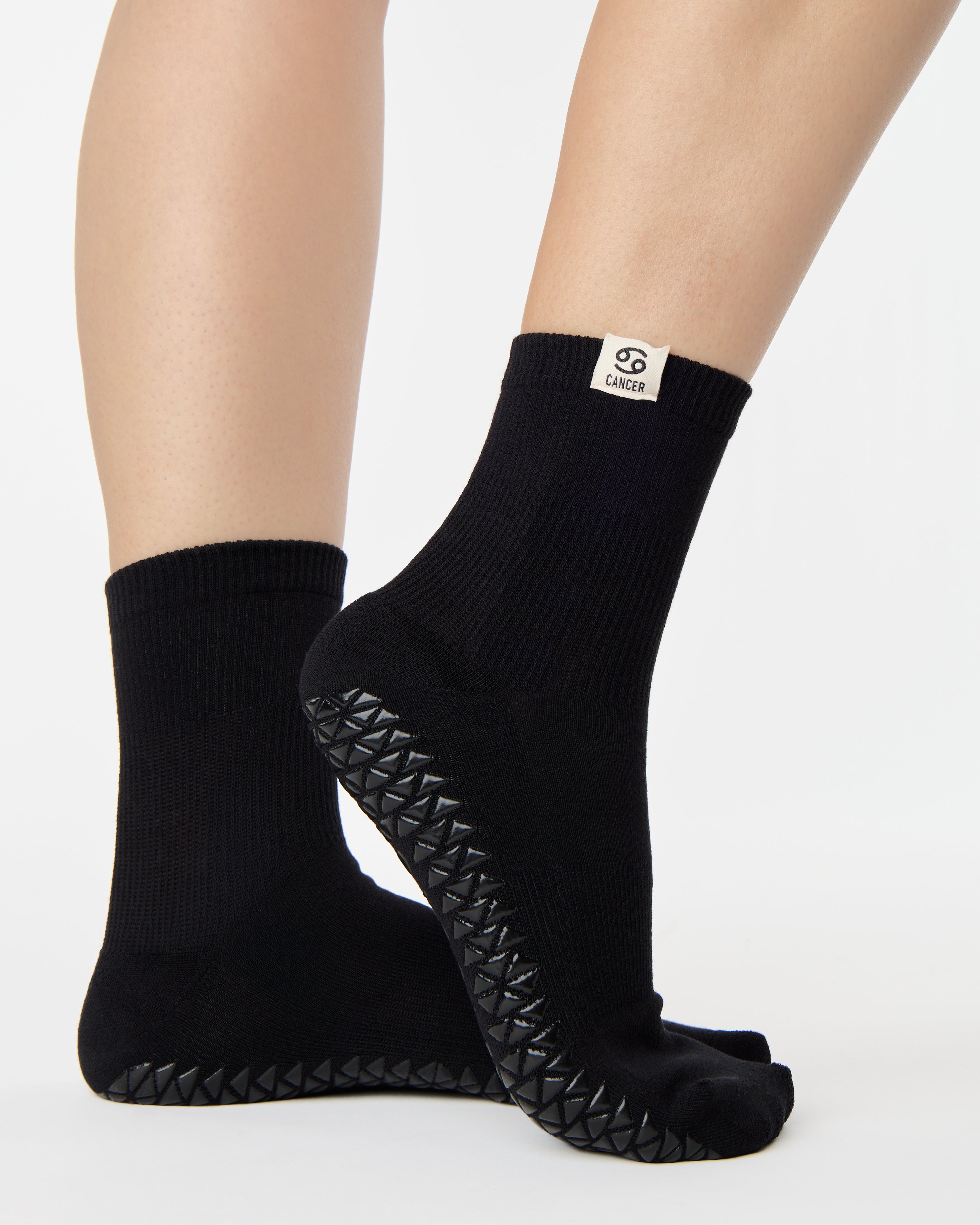 Woman wearing a solid black ankle grip sock with cancer zodiac sign embroidered on the side. Made for pilates, barre, yoga, and beyond. 