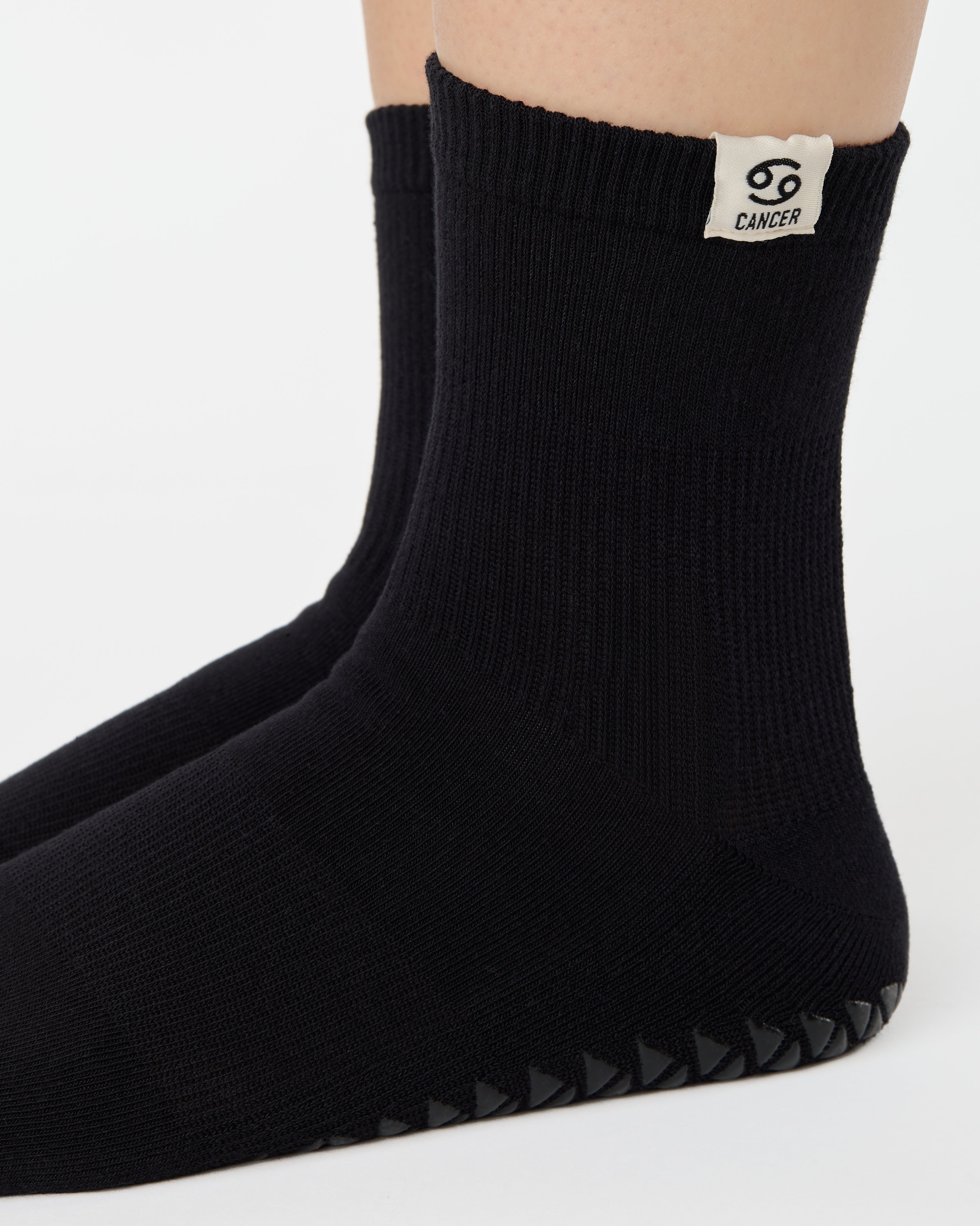 Woman wearing a solid black ankle grip sock with cancer zodiac sign embroidered on the side. Made for pilates, barre, yoga, and beyond. 