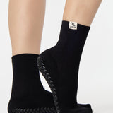 Woman wearing a solid black ankle grip sock with capricorn zodiac sign embroidered on the side. Made for pilates, barre, yoga, and beyond. 