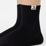 Woman wearing a solid black ankle grip sock with capricorn zodiac sign embroidered on the side. Made for pilates, barre, yoga, and beyond. 