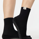 Woman wearing a solid black ankle grip sock with gemini zodiac sign embroidered on the side. Made for pilates, barre, yoga, and beyond. 