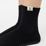 Woman wearing a solid black ankle grip sock with gemini zodiac sign embroidered on the side. Made for pilates, barre, yoga, and beyond. 