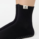 Woman wearing a solid black ankle grip sock with gemini zodiac sign embroidered on the side. Made for pilates, barre, yoga, and beyond. 
