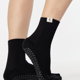 Woman wearing a solid black ankle grip sock with leo zodiac sign embroidered on the side. Made for pilates, barre, yoga, and beyond. 