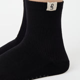 Woman wearing a solid black ankle grip sock with leo zodiac sign embroidered on the side. Made for pilates, barre, yoga, and beyond. 