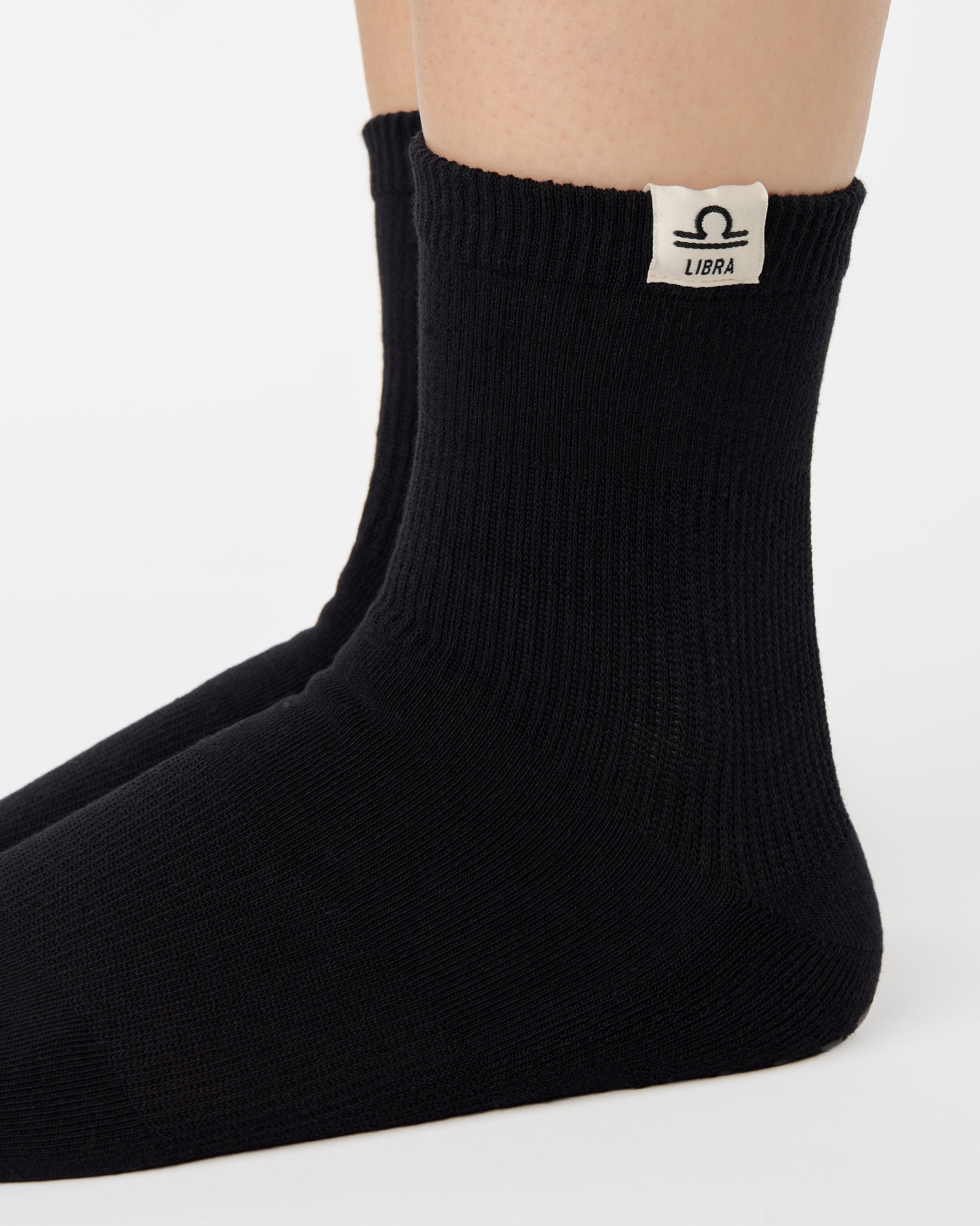 Woman wearing a solid black ankle grip sock with libra zodiac sign embroidered on the side. Made for pilates, barre, yoga, and beyond. 