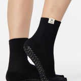 Woman wearing a solid black ankle grip sock with pisces zodiac sign embroidered on the side. Made for pilates, barre, yoga, and beyond. 