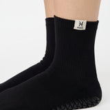 Woman wearing a solid black ankle grip sock with pisces zodiac sign embroidered on the side. Made for pilates, barre, yoga, and beyond. 