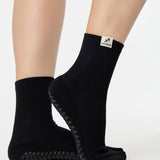 Woman wearing a solid black ankle grip sock with sagittarius zodiac sign embroidered on the side. Made for pilates, barre, yoga, and beyond. 