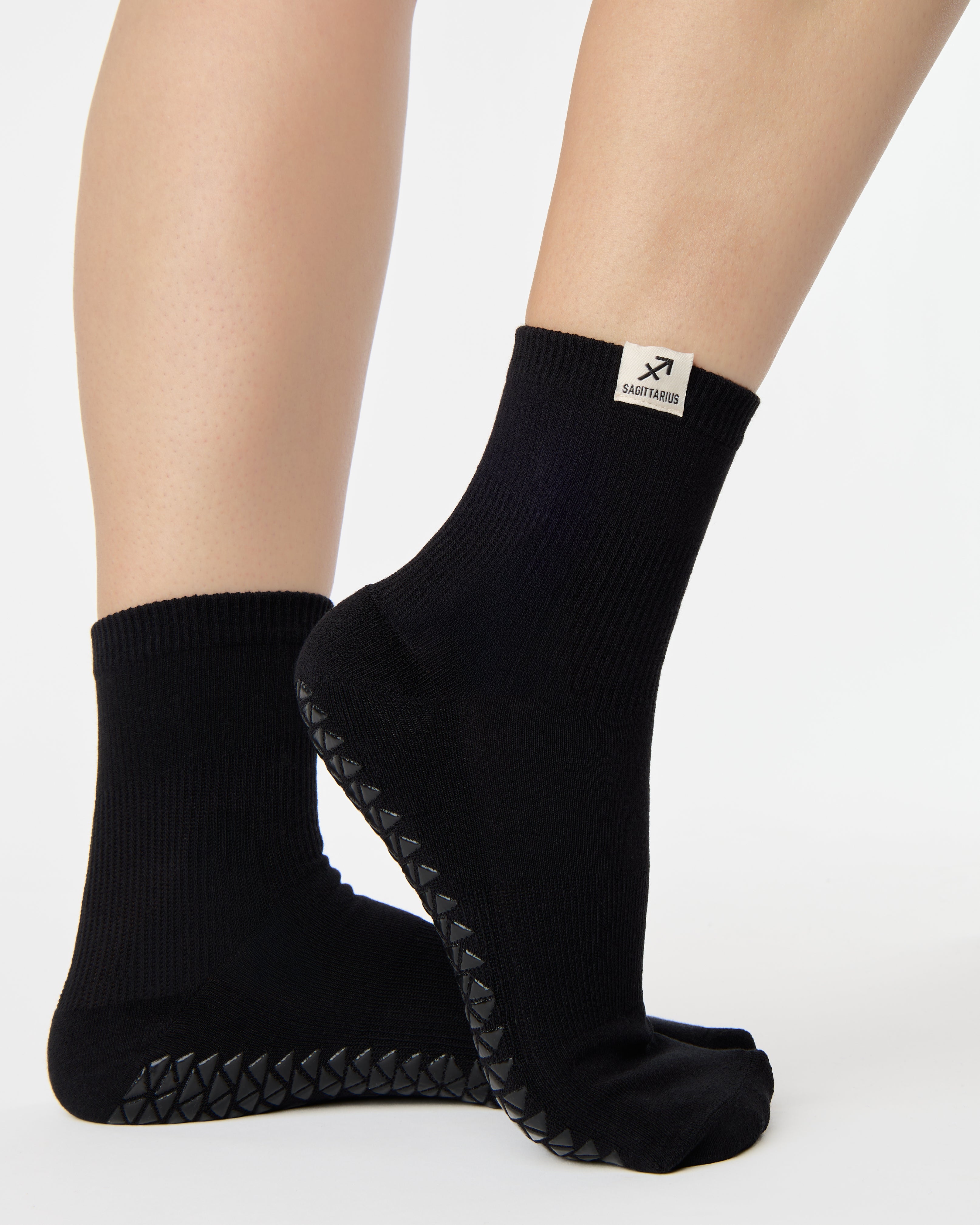 Woman wearing a solid black ankle grip sock with sagittarius zodiac sign embroidered on the side. Made for pilates, barre, yoga, and beyond. 