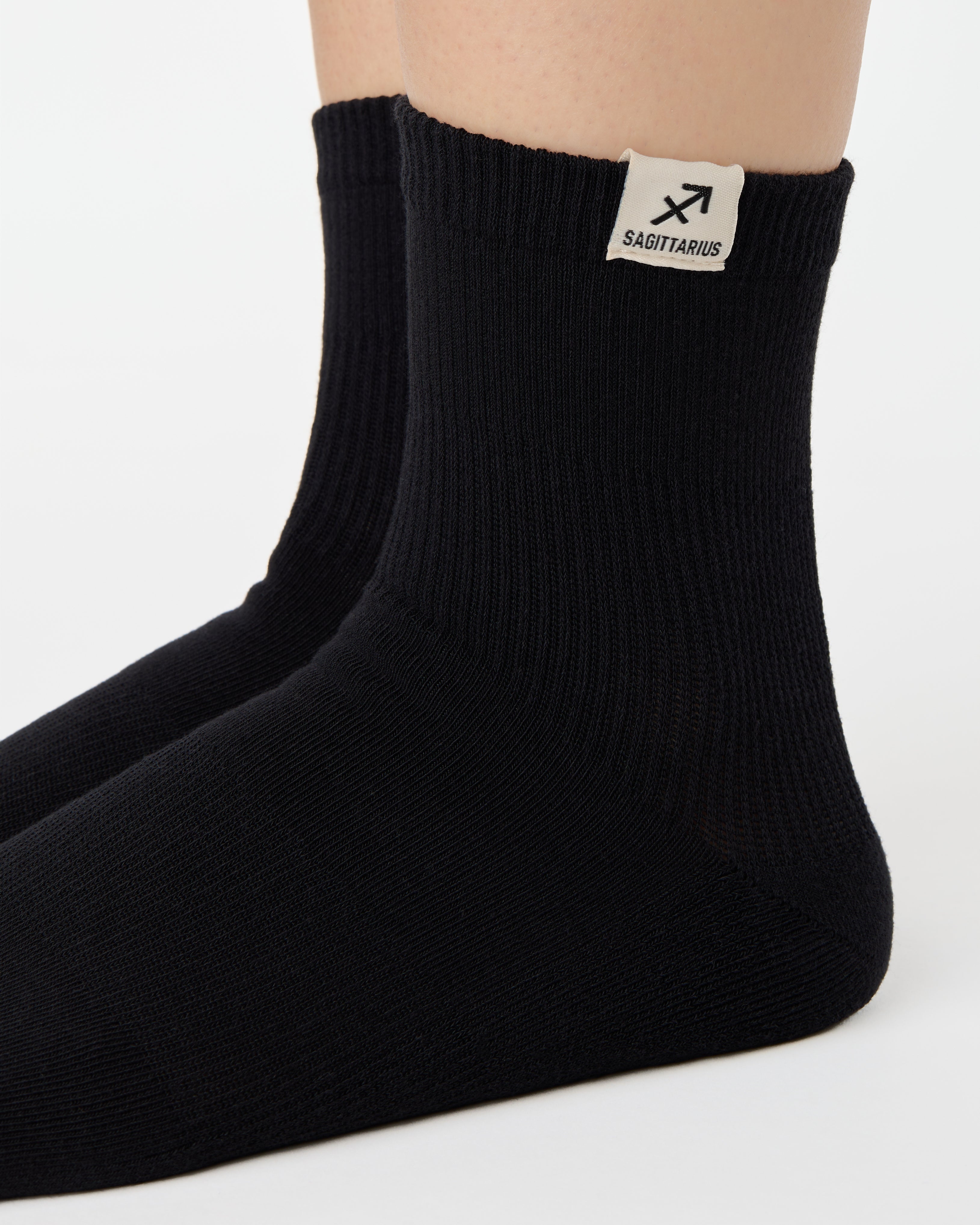 Woman wearing a solid black ankle grip sock with sagittarius zodiac sign embroidered on the side. Made for pilates, barre, yoga, and beyond. 