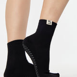 Woman wearing a solid black ankle grip sock with scorpio zodiac sign embroidered on the side. Made for pilates, barre, yoga, and beyond. 
