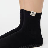 Woman wearing a solid black ankle grip sock with scorpio zodiac sign embroidered on the side. Made for pilates, barre, yoga, and beyond. 