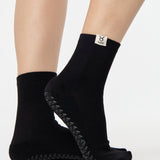 Woman wearing a solid black ankle grip sock with taurus zodiac sign embroidered on the side. Made for pilates, barre, yoga, and beyond. 