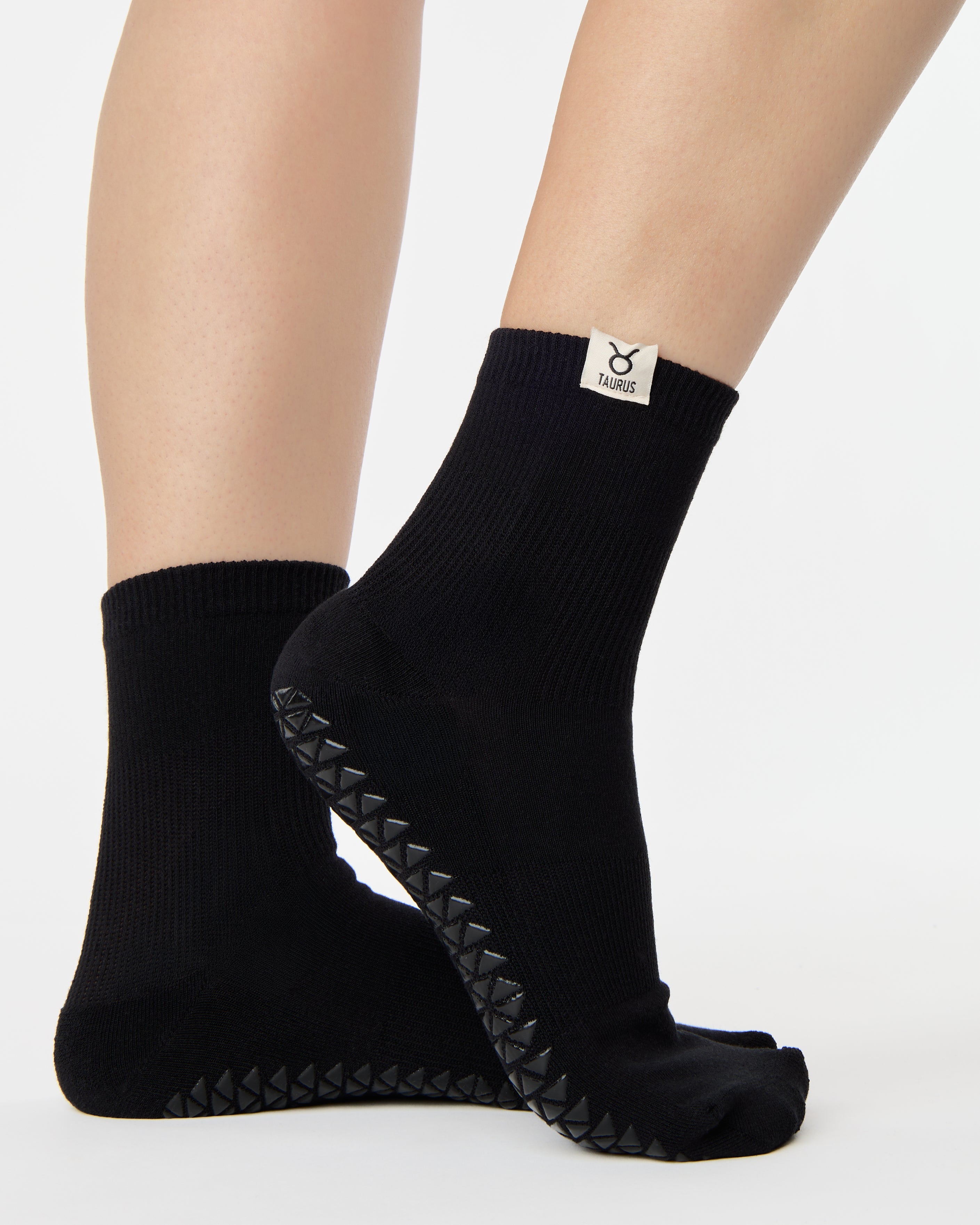 Woman wearing a solid black ankle grip sock with taurus zodiac sign embroidered on the side. Made for pilates, barre, yoga, and beyond. 