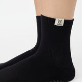 Woman wearing a solid black ankle grip sock with taurus zodiac sign embroidered on the side. Made for pilates, barre, yoga, and beyond. 