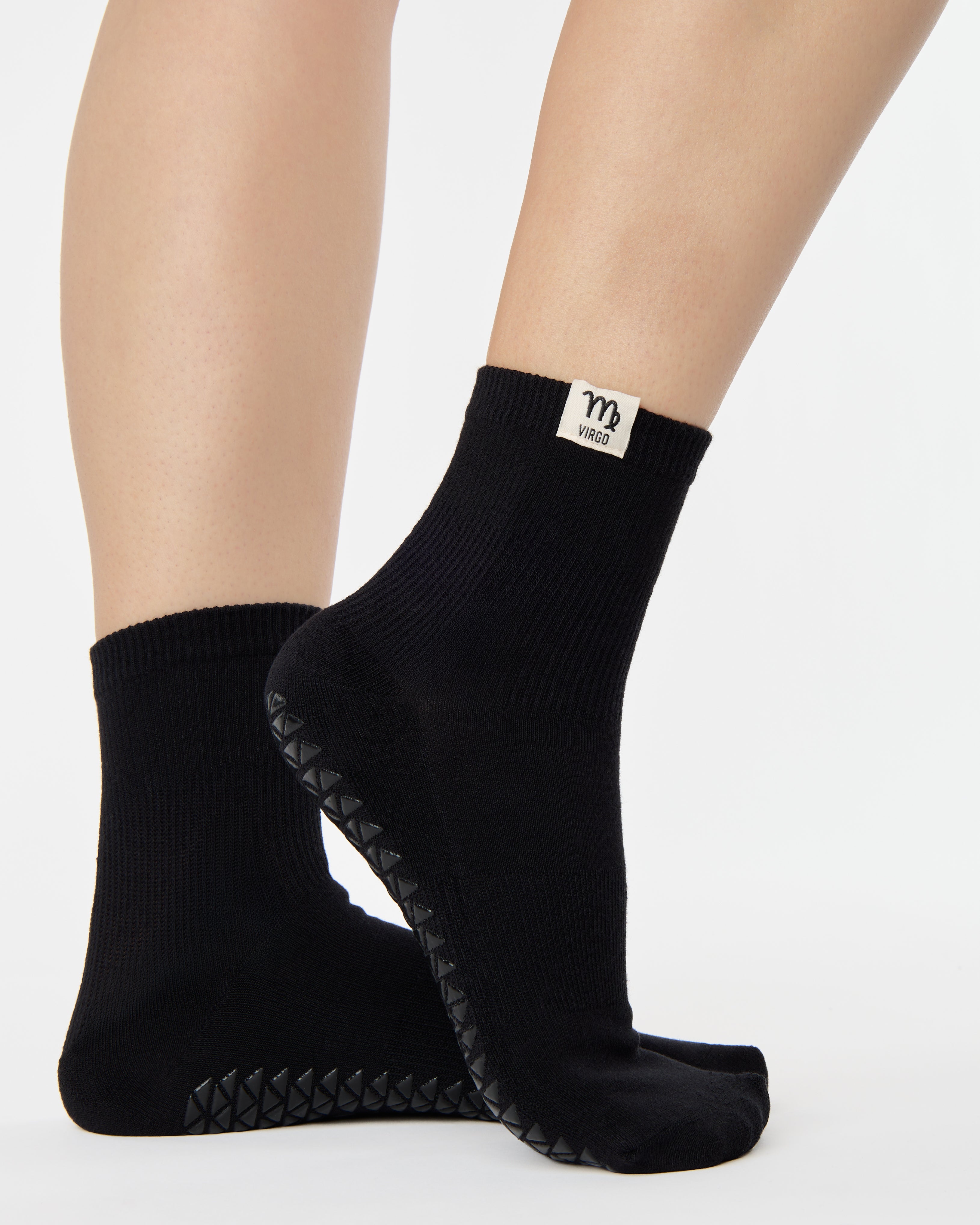Woman wearing a solid black ankle grip sock with virgo zodiac sign embroidered on the side. Made for pilates, barre, yoga, and beyond. 