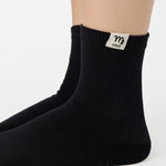 Woman wearing a solid black ankle grip sock with virgo zodiac sign embroidered on the side. Made for pilates, barre, yoga, and beyond. 