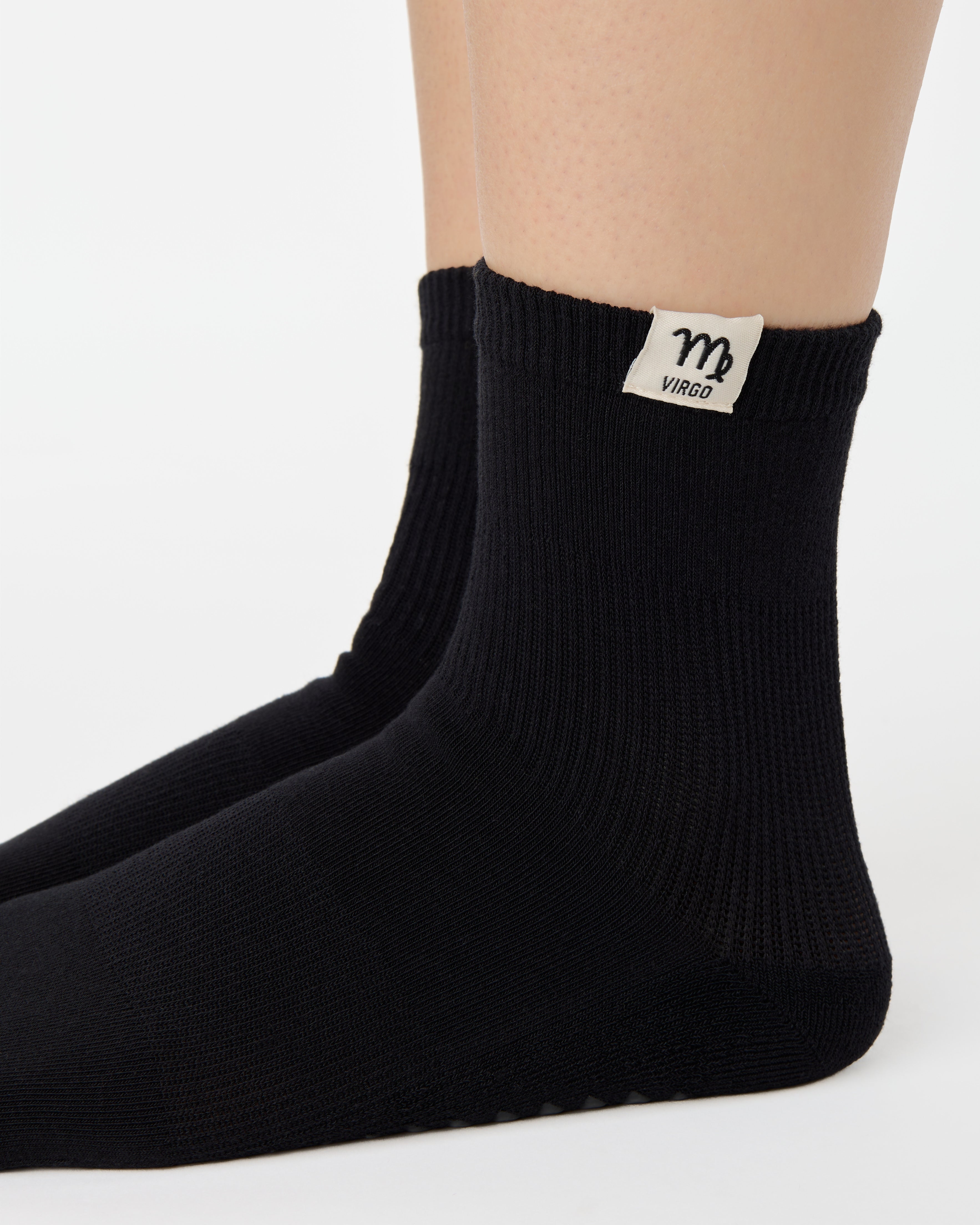 Woman wearing a solid black ankle grip sock with virgo zodiac sign embroidered on the side. Made for pilates, barre, yoga, and beyond. 