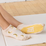 Women on a yoga mat wearing an off white full foot grip sock with bananas string of red hearts , made for pilates, barre, yoga, and beyond.