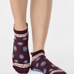 Woman wearing a full foot grip sock that has the design of a classic bandana, in the hues brown cherry and blue and beige detailing. Made for pilates, barre, yoga and beyond. 