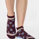 Woman wearing a full foot grip sock that has the design of a classic bandana, in the hues brown cherry and blue and beige detailing. Made for pilates, barre, yoga and beyond. 
