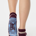 Woman wearing a full foot grip sock that has the design of a classic bandana, in the hues brown cherry and blue and beige detailing. Made for pilates, barre, yoga and beyond. 