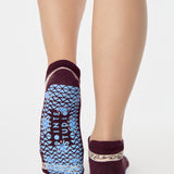 Woman wearing a full foot grip sock that has the design of a classic bandana, in the hues brown cherry and blue and beige detailing. Made for pilates, barre, yoga and beyond. 