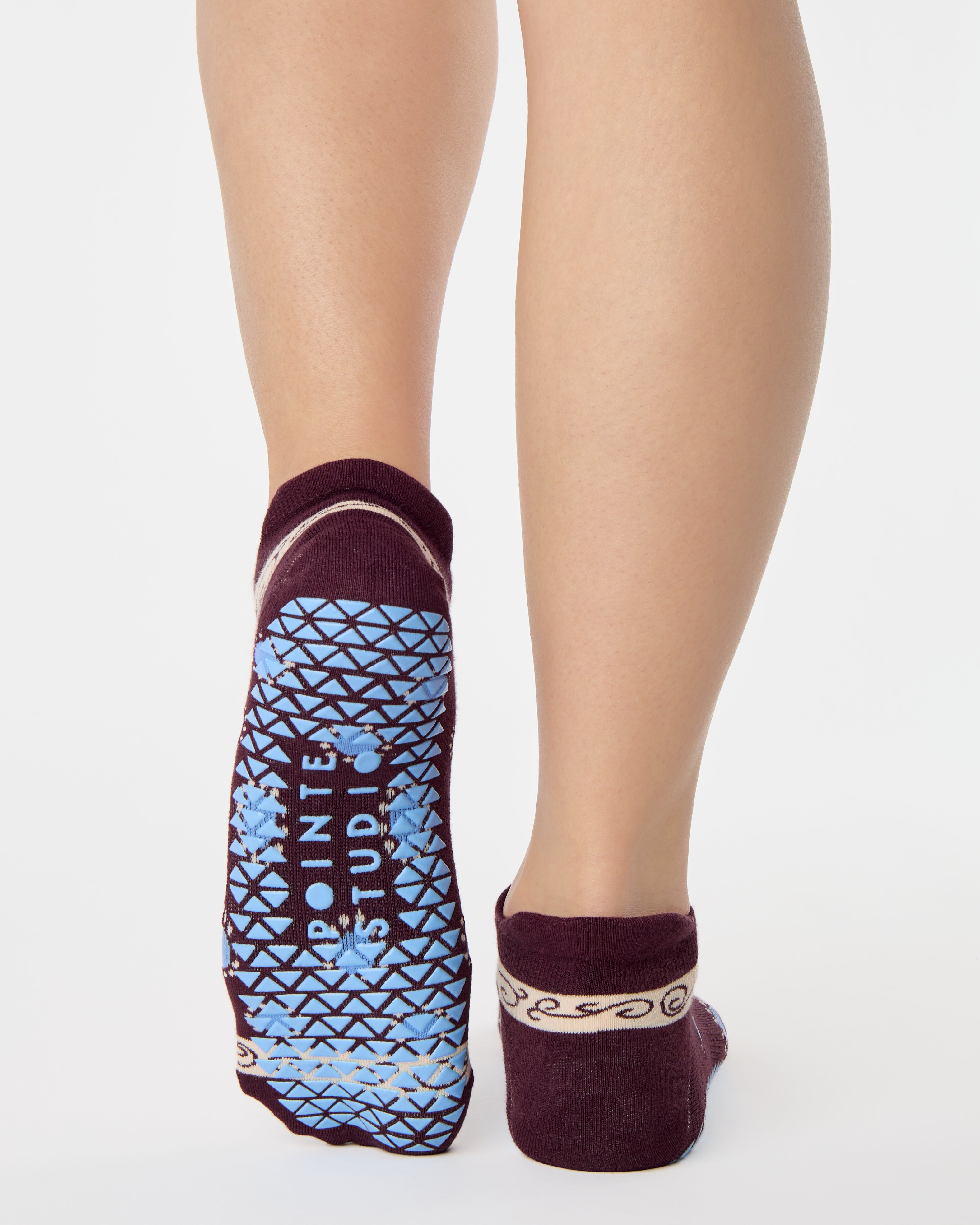 Woman wearing a full foot grip sock that has the design of a classic bandana, in the hues brown cherry and blue and beige detailing. Made for pilates, barre, yoga and beyond. 