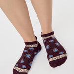 Woman wearing a full foot grip sock that has the design of a classic bandana, in the hues brown cherry and blue and beige detailing. Made for pilates, barre, yoga and beyond. 