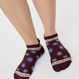 Woman wearing a full foot grip sock that has the design of a classic bandana, in the hues brown cherry and blue and beige detailing. Made for pilates, barre, yoga and beyond. 
