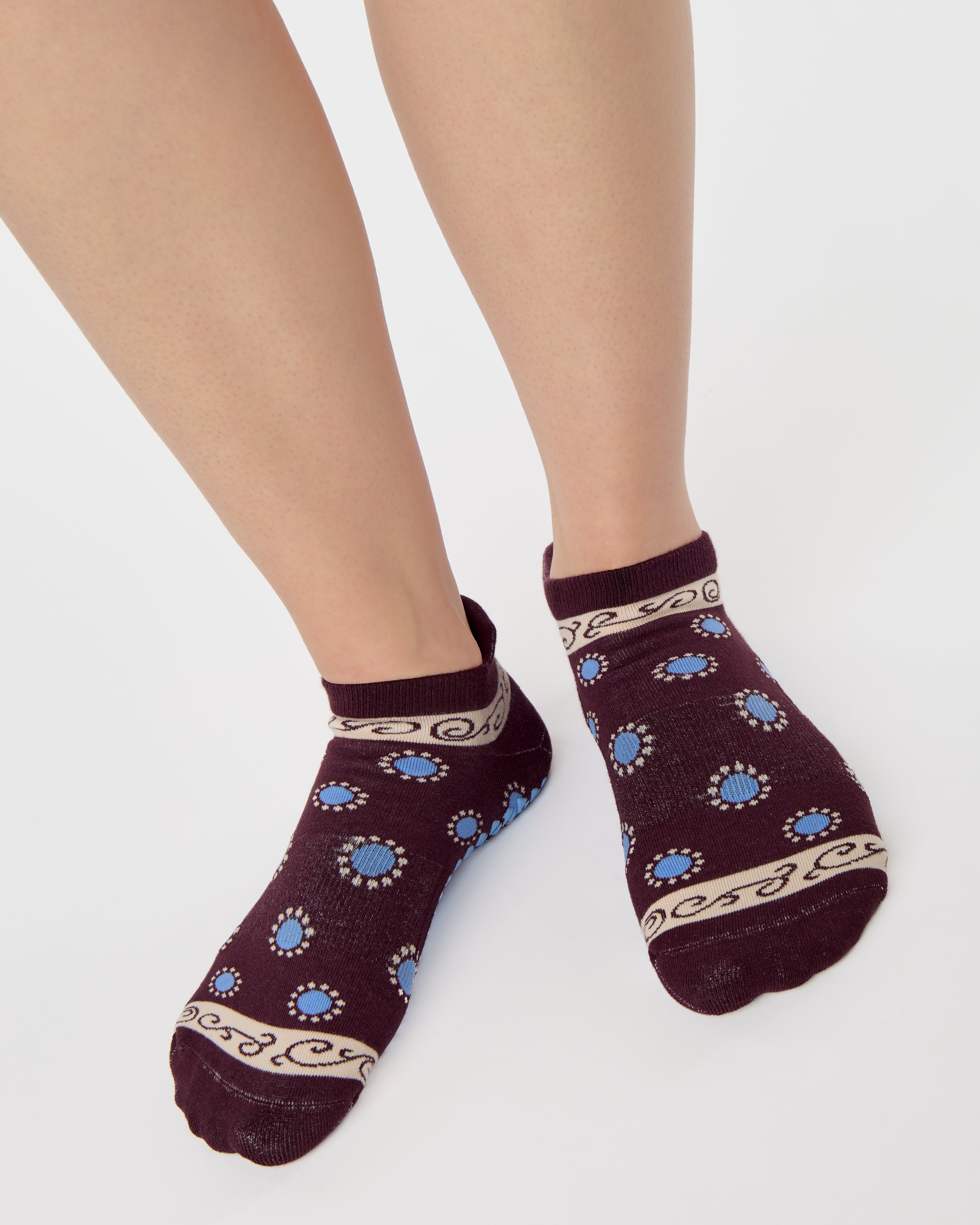 Woman wearing a full foot grip sock that has the design of a classic bandana, in the hues brown cherry and blue and beige detailing. Made for pilates, barre, yoga and beyond. 