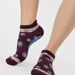 Woman wearing a full foot grip sock that has the design of a classic bandana, in the hues brown cherry and blue and beige detailing. Made for pilates, barre, yoga and beyond. 