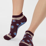 Woman wearing a full foot grip sock that has the design of a classic bandana, in the hues brown cherry and blue and beige detailing. Made for pilates, barre, yoga and beyond. 