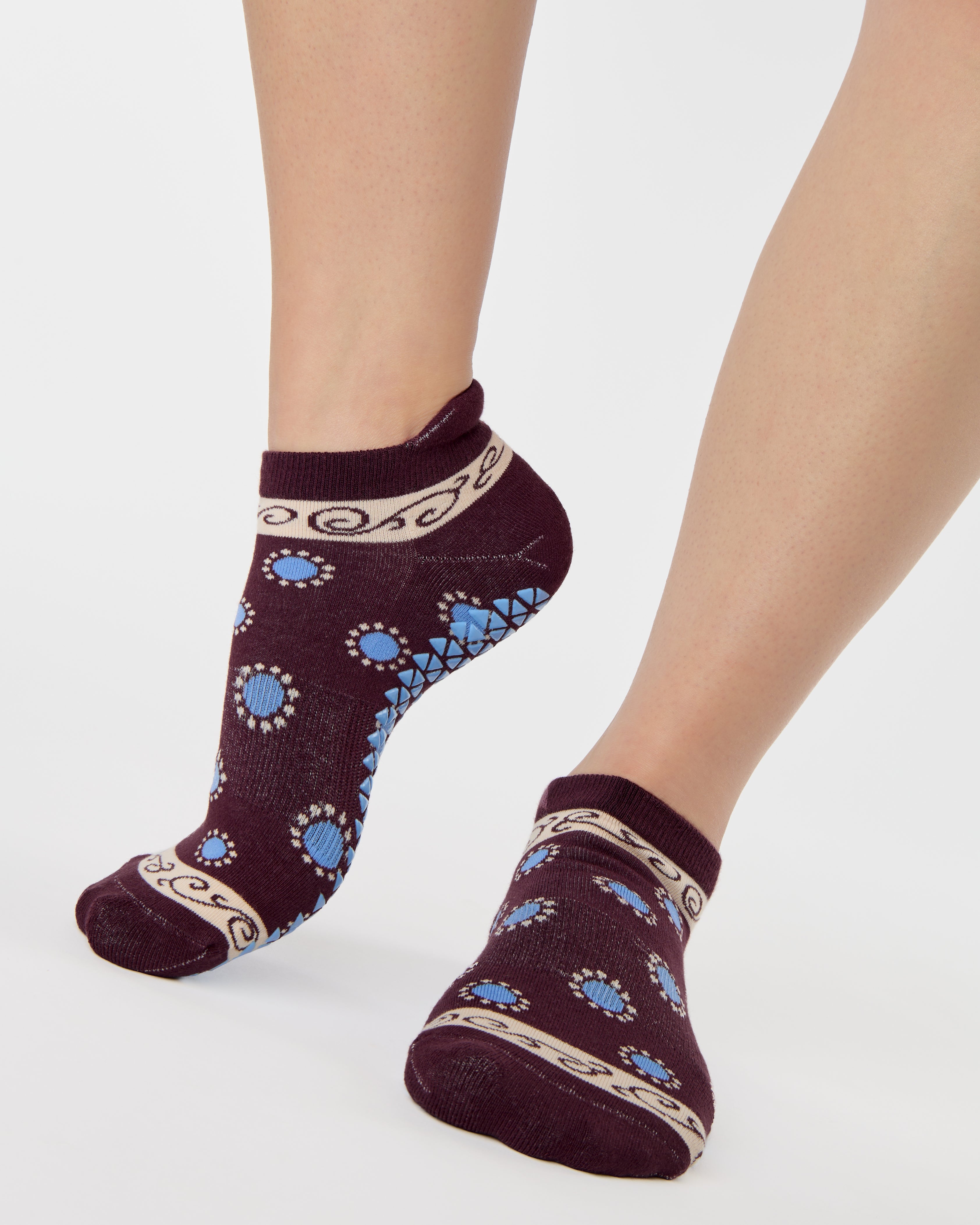 Woman wearing a full foot grip sock that has the design of a classic bandana, in the hues brown cherry and blue and beige detailing. Made for pilates, barre, yoga and beyond. 