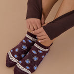 Woman wearing a full foot grip sock that has the design of a classic bandana, in the hues brown cherry and blue and beige detailing. Made for pilates, barre, yoga and beyond. 