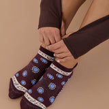 Woman wearing a full foot grip sock that has the design of a classic bandana, in the hues brown cherry and blue and beige detailing. Made for pilates, barre, yoga and beyond. 