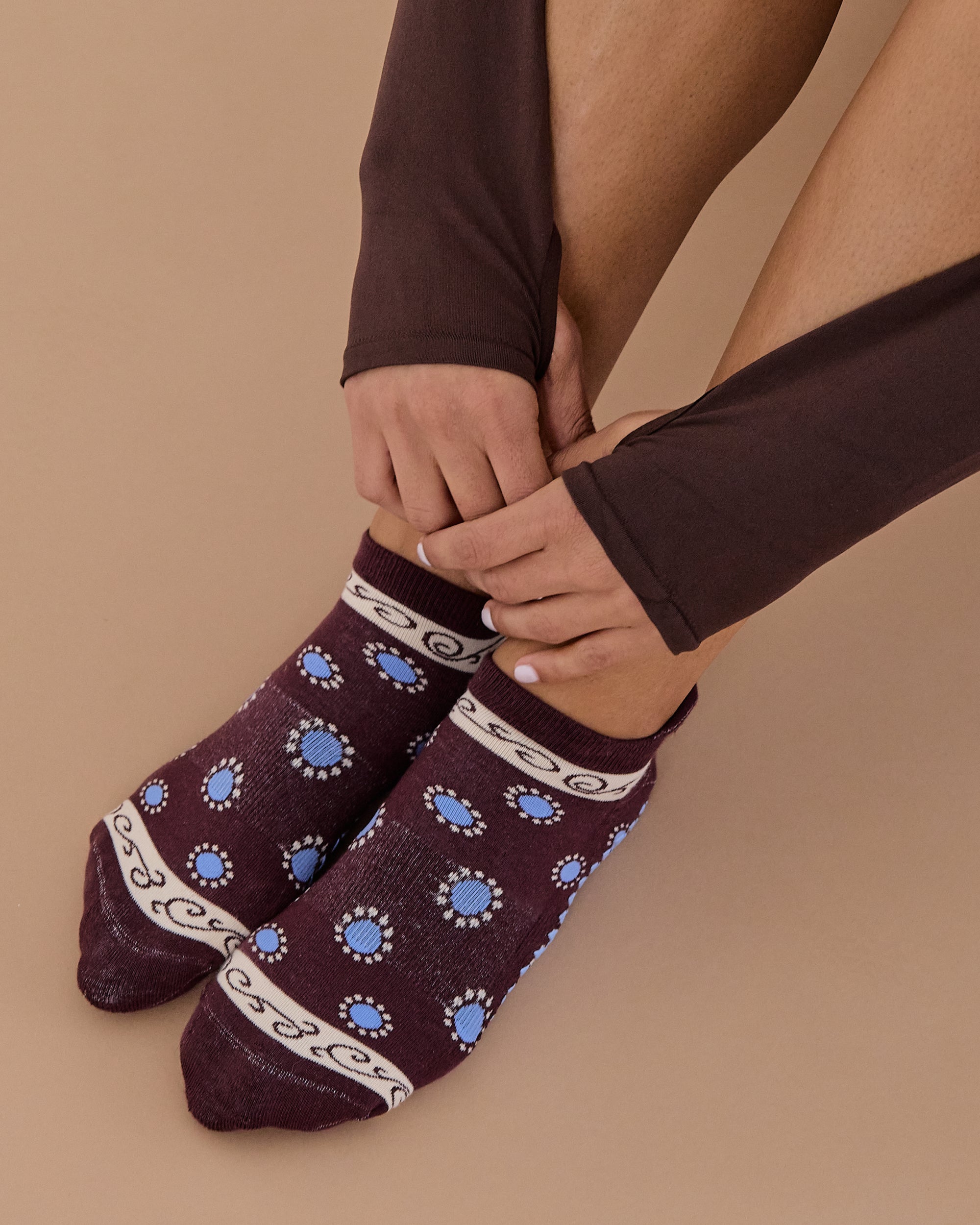 Woman wearing a full foot grip sock that has the design of a classic bandana, in the hues brown cherry and blue and beige detailing. Made for pilates, barre, yoga and beyond. 