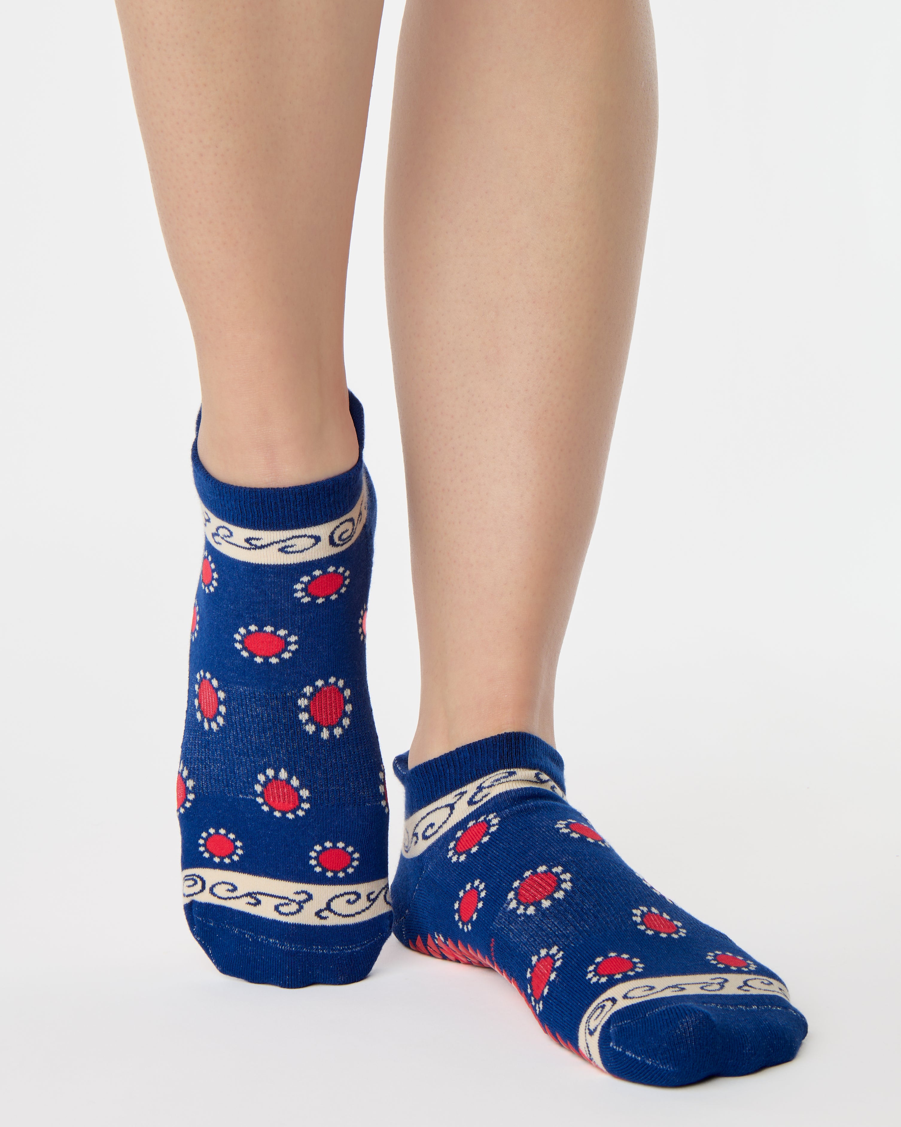 Woman wearing a full foot grip sock that has the design of a classic bandana, in a blue hue with red and white detailing. Made for pilates, barre, yoga and beyond. 