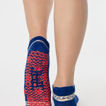 Woman wearing a full foot grip sock that has the design of a classic bandana, in a blue hue with red and white detailing. Made for pilates, barre, yoga and beyond. 