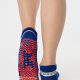 Woman wearing a full foot grip sock that has the design of a classic bandana, in a blue hue with red and white detailing. Made for pilates, barre, yoga and beyond. 