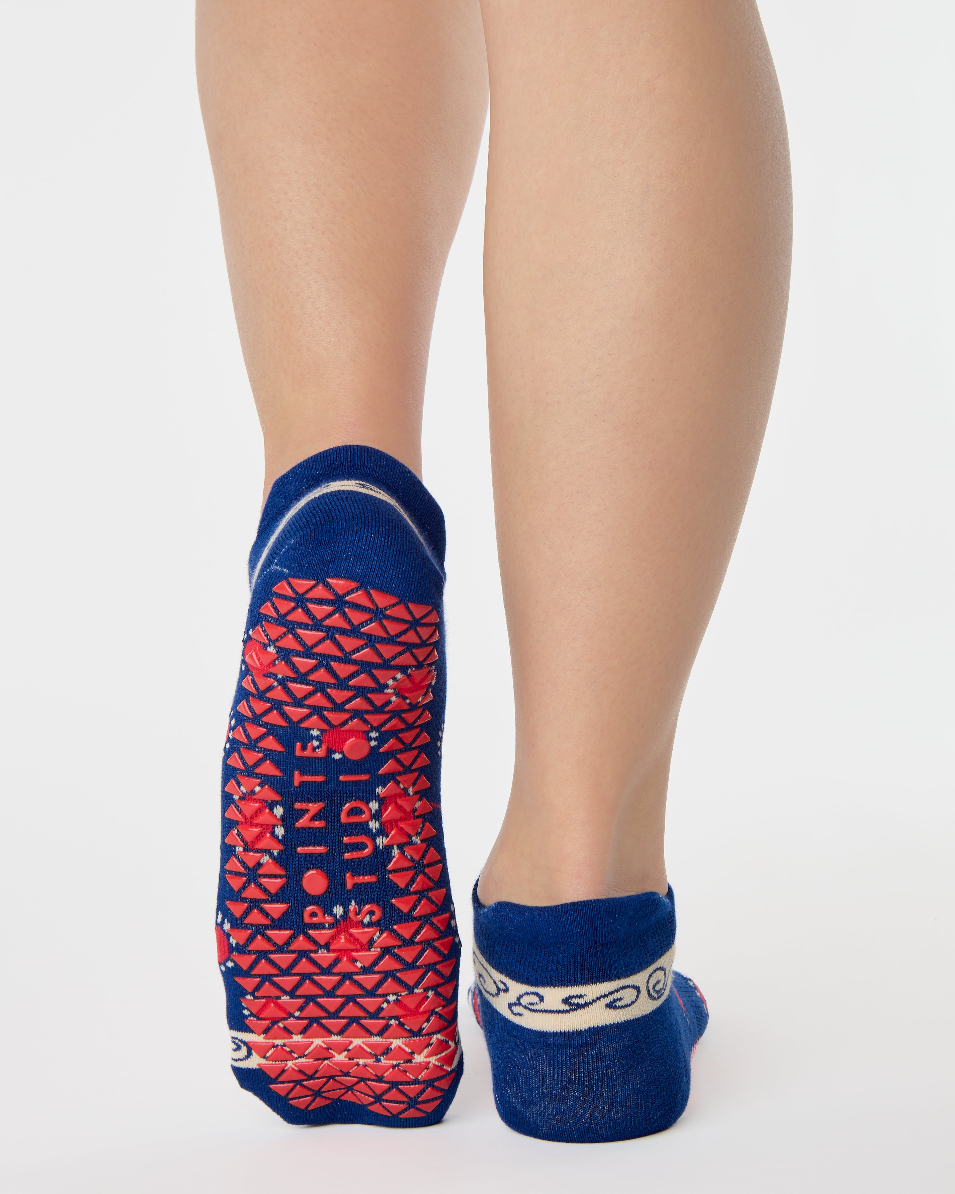 Woman wearing a full foot grip sock that has the design of a classic bandana, in a blue hue with red and white detailing. Made for pilates, barre, yoga and beyond. 