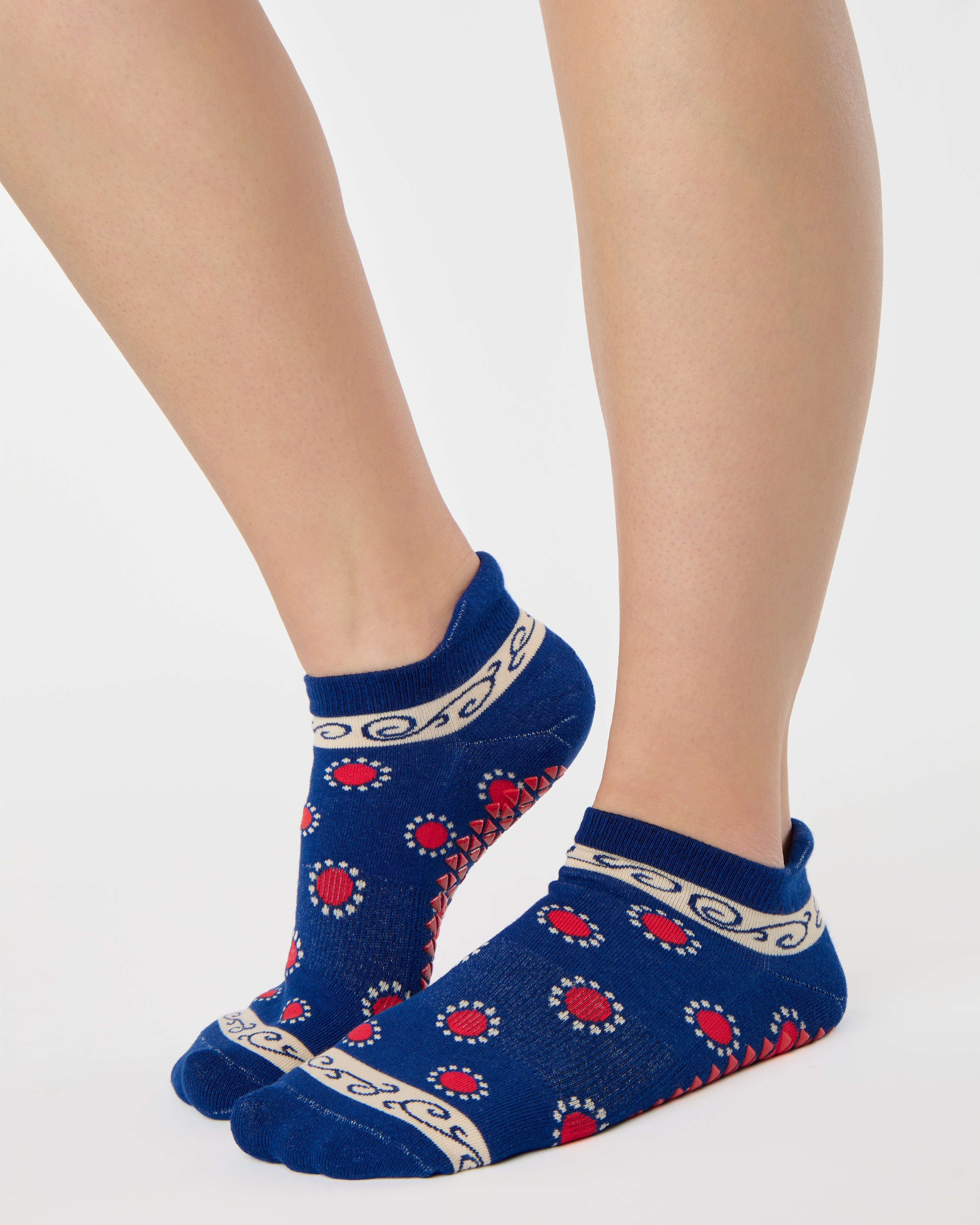 Woman wearing a full foot grip sock that has the design of a classic bandana, in a blue hue with red and white detailing. Made for pilates, barre, yoga and beyond. 