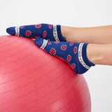 Woman wearing a full foot grip sock that has the design of a classic bandana, in a blue hue with red and white detailing. Made for pilates, barre, yoga and beyond. 